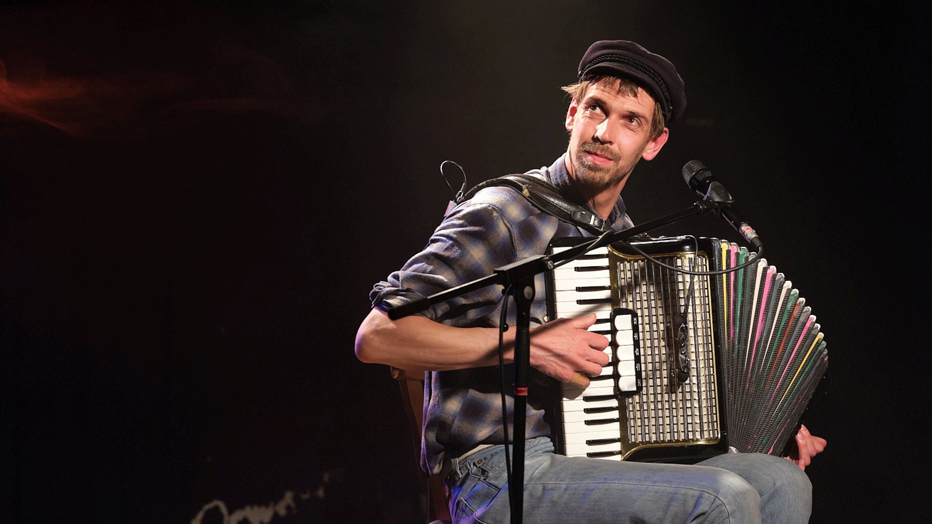 Maxi Pongratz mit Schiebermütze spielt Akkordeon auf Konzertbühne vor Mikrofon unter warmem Scheinwerferlicht