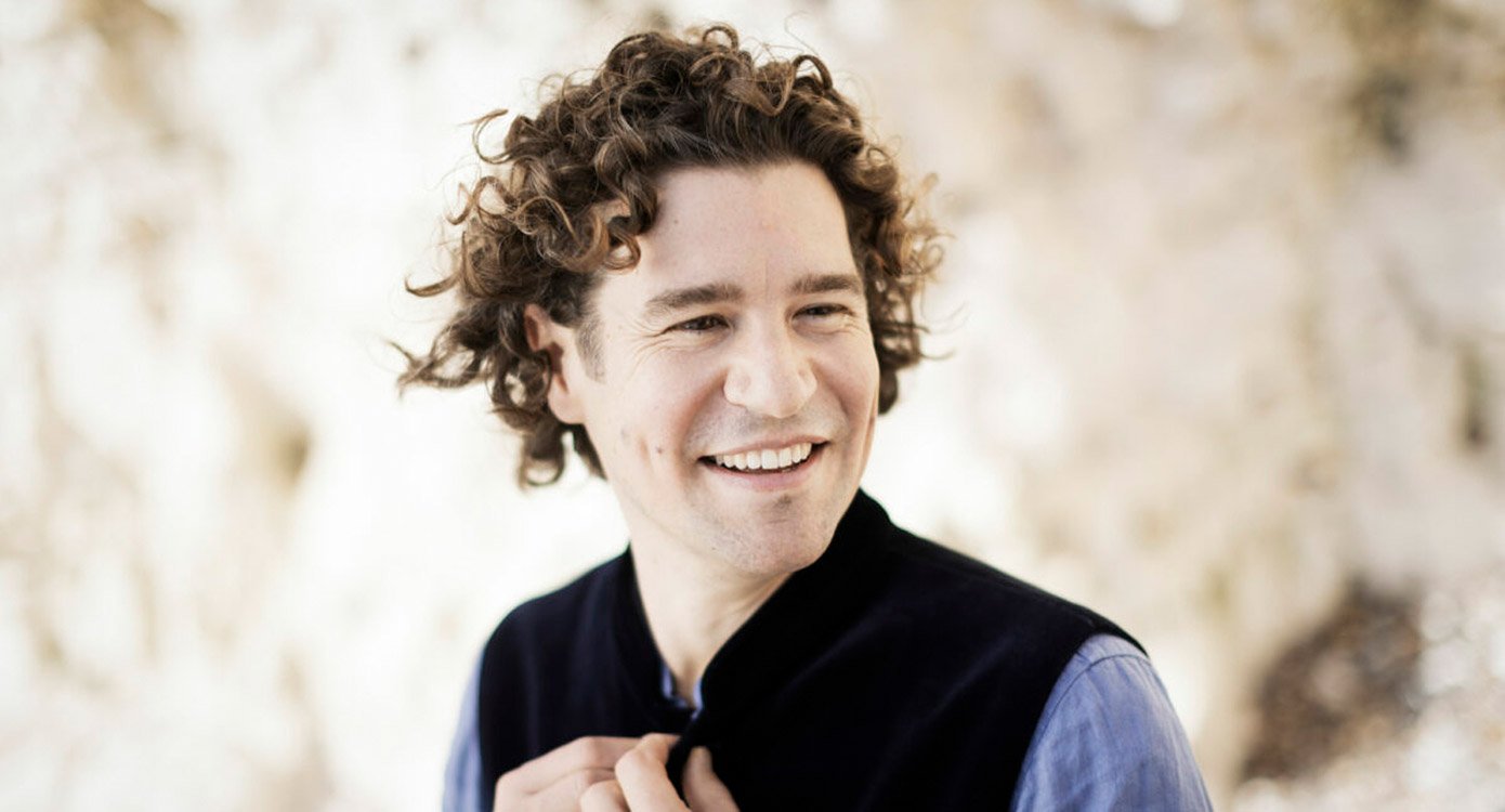 Mann mit dunklen Locken, blauem Hemd und schwarzer Weste, lachend