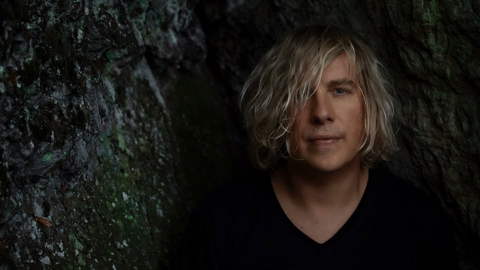 Foto für das Event von Dominik Eulberg, mit einem Bild des Künstlers vor einer Fels- bzw. steinartigen Textur im Hintergrund