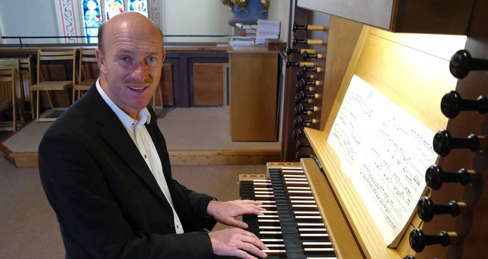 Mann in schwarzem Anzug an Orgel sitzend
