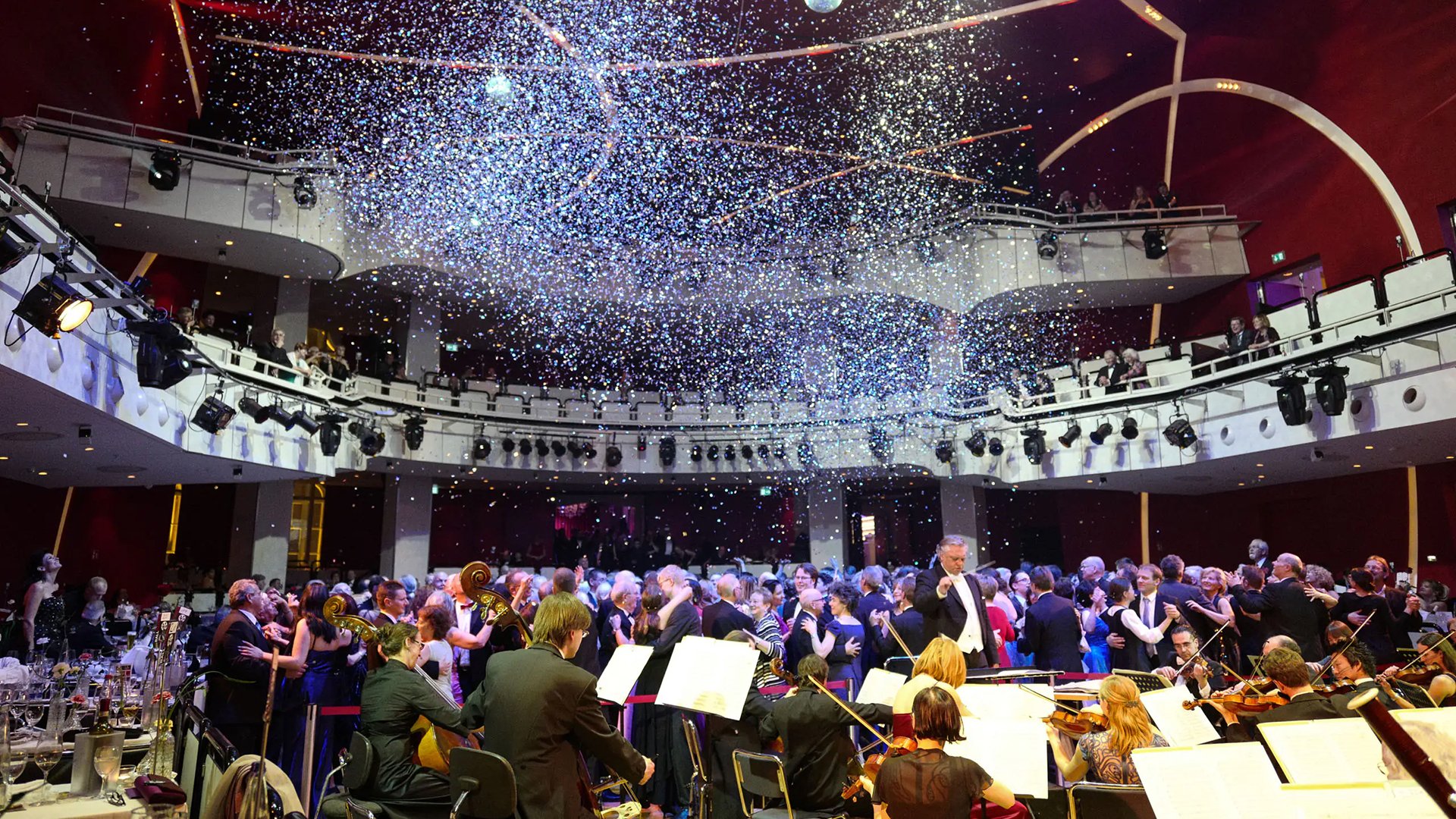 Ein Foto für das Event Ball der Sterne, mit Orchester, tanzenden Menschen und Konfetti.