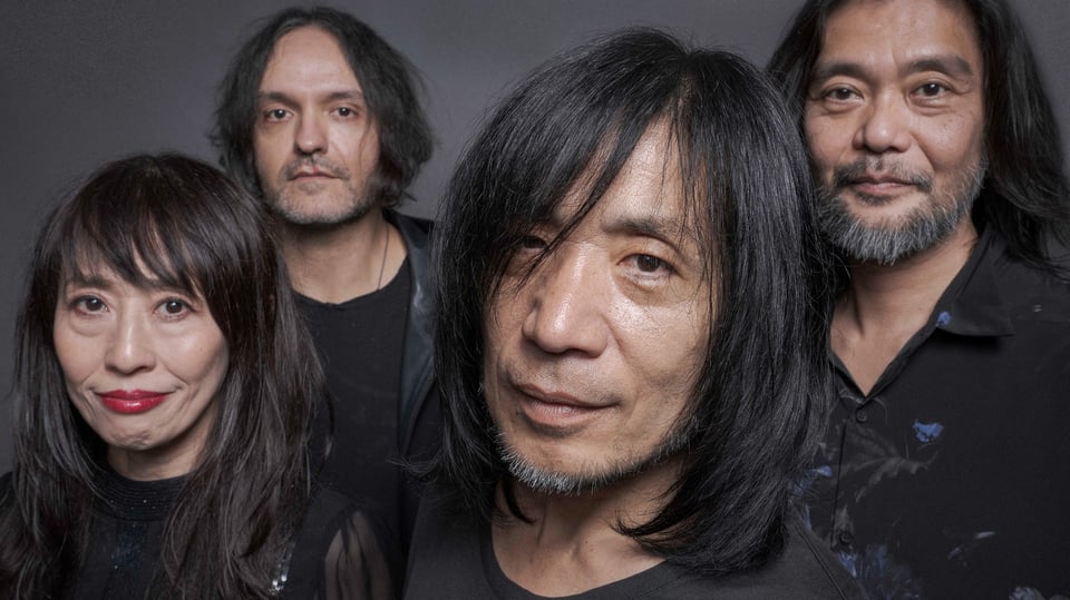 Fünf Mitglieder der Band MONO, dunkel gekleidet, stehen eng beieinander vor neutral grauem Hintergrund