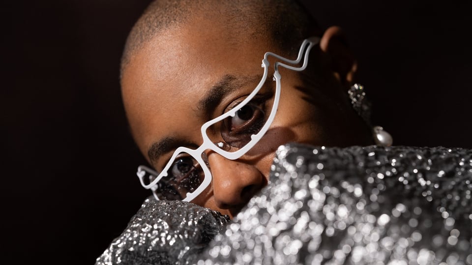 Ein Foto der Künstlerin CECILE McLORIN SALVANT mit einer weißen futuristischen Brille und silber glänzender Kleidung