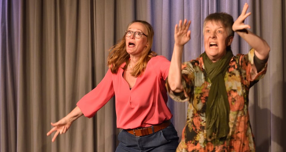 Zwei Frauen vor einem Bühnenhintergrund mit Vorhängen – Szene aus dem Theaterstück ‚Die dritte Reise ins Ungewisse…‘ von Die Spontanitäter