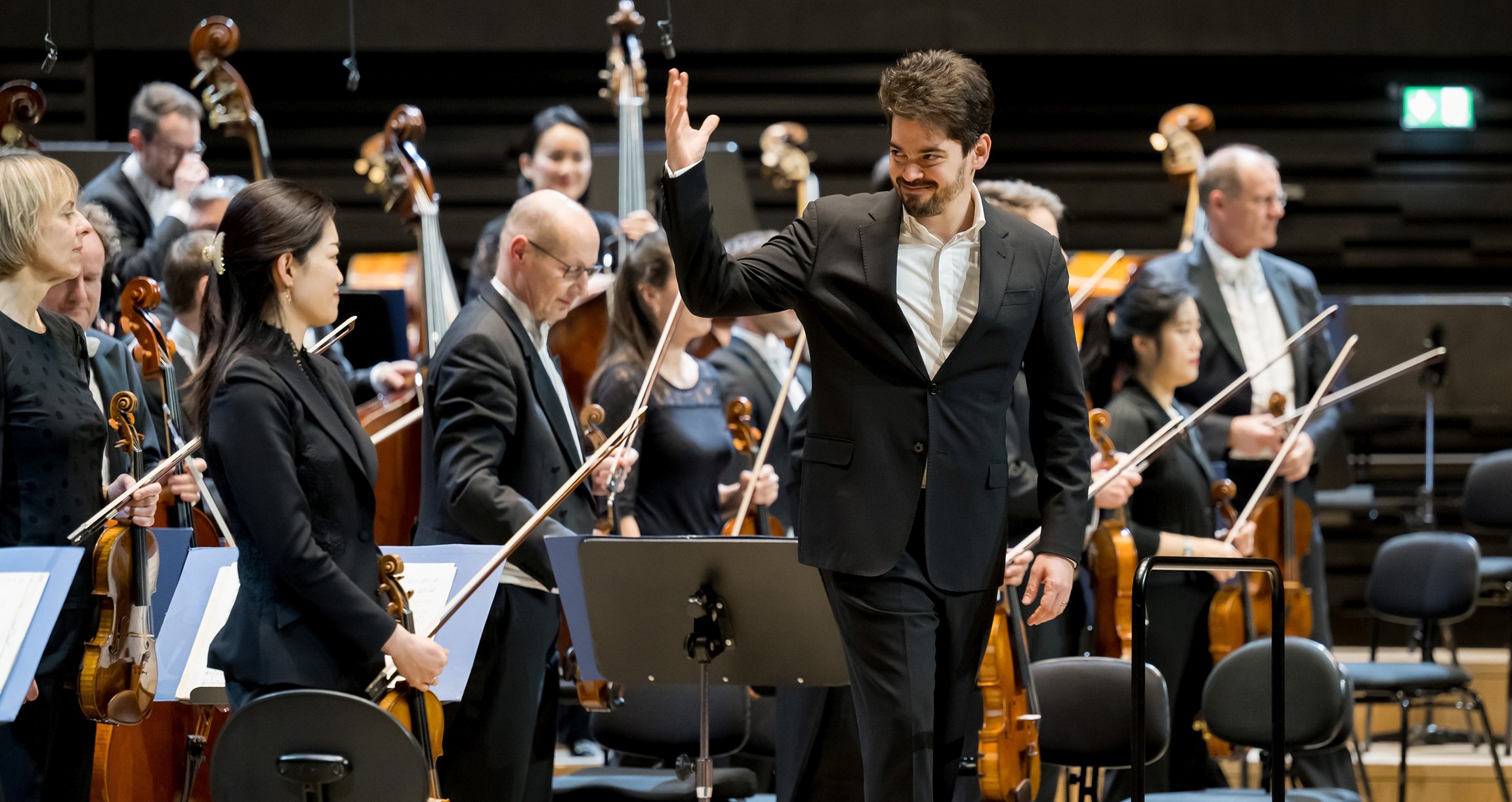 Foto eines winkenden Jungen und von Mitgliedern eines Orchesters mit Instrumenten im Hintergrund