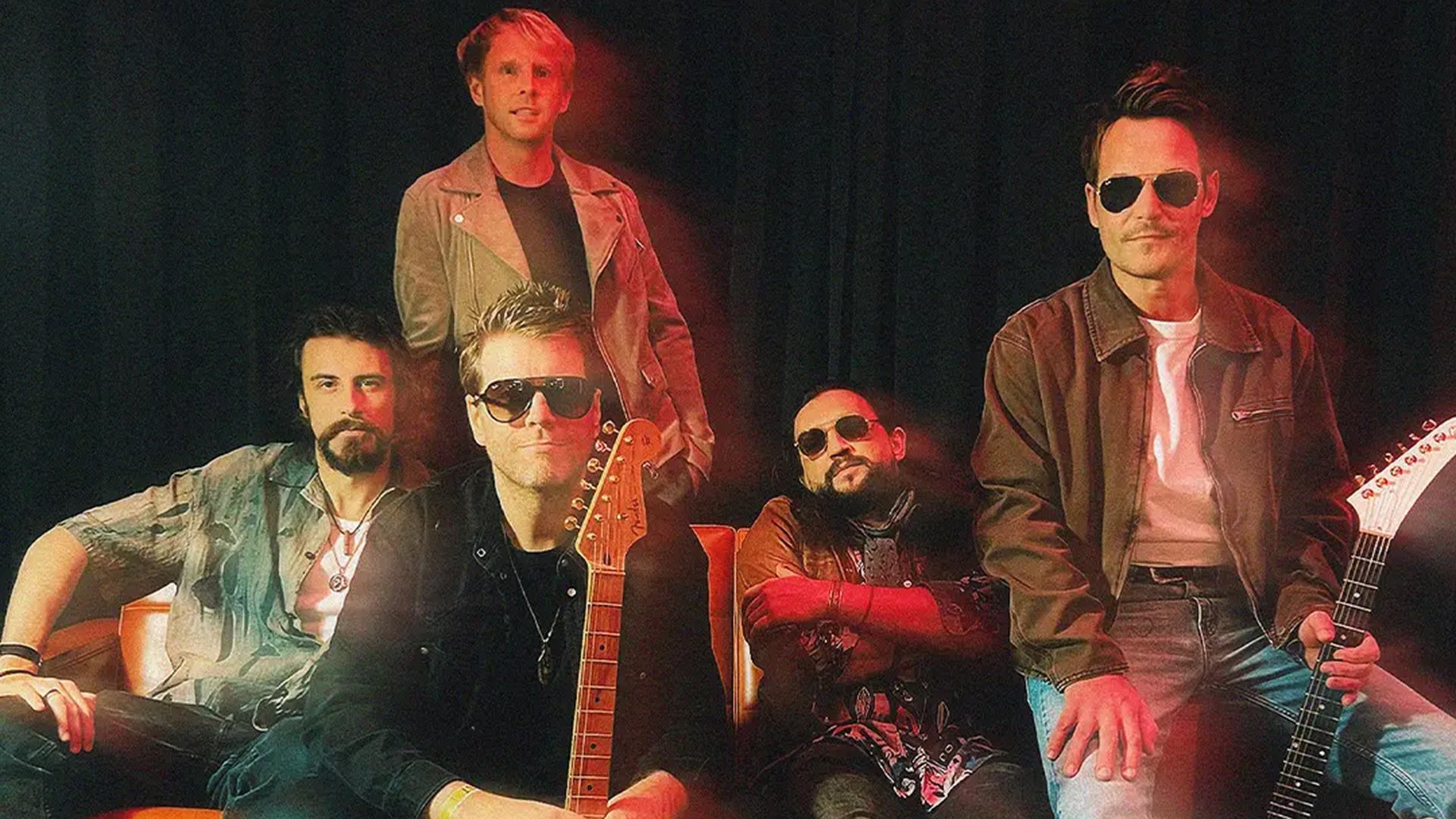 Der Künstler Danny Bryant mit Band auf einem Sofa, einige Personen tragen Sonnenbrillen, in farbigem Scheinwerferlicht vor einem dunklen Vorhang