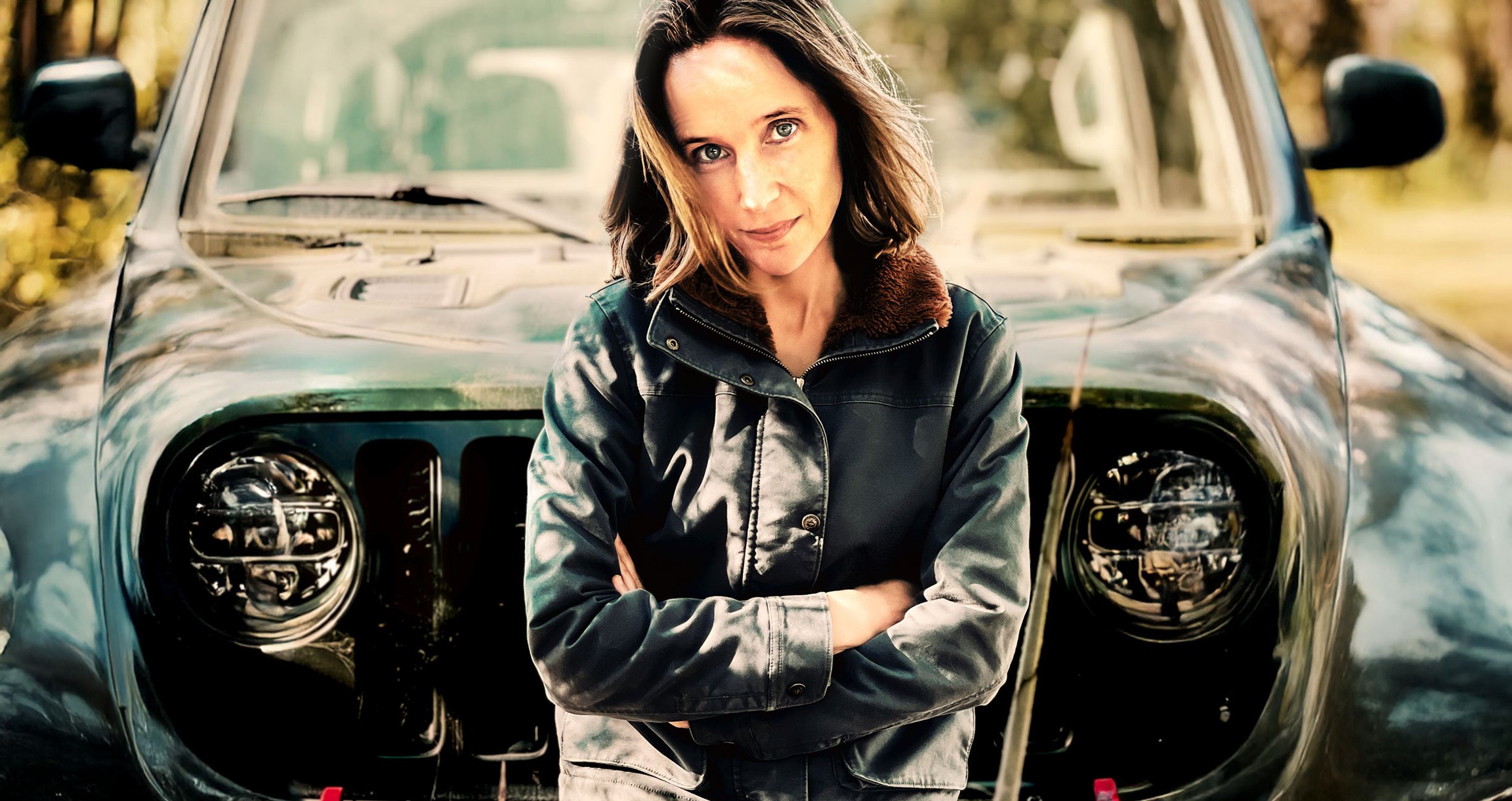 Dame mit braunen Haaren und schwarzer Lederjacke an Oldtimer lehnend