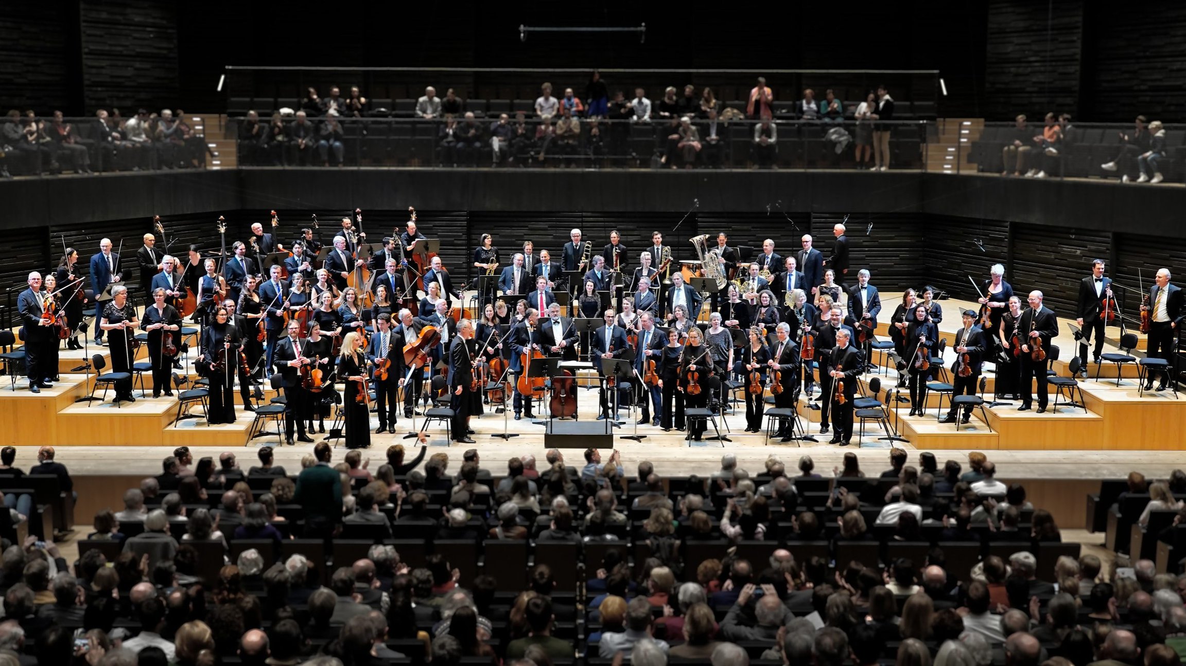 Bild von Orchester auf Bühne mit Publikum