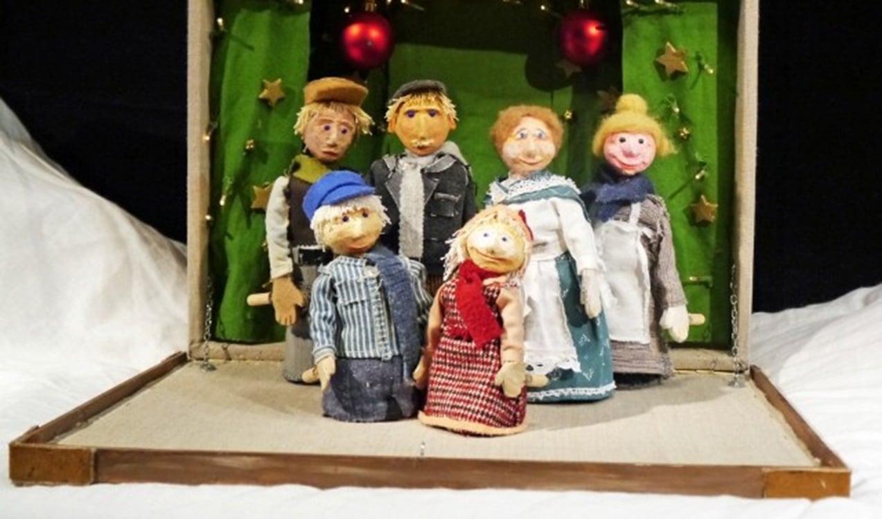 sechs Puppenfiguren aufgestellt in einem Holzkoffer vor Weihnachtsdekoration