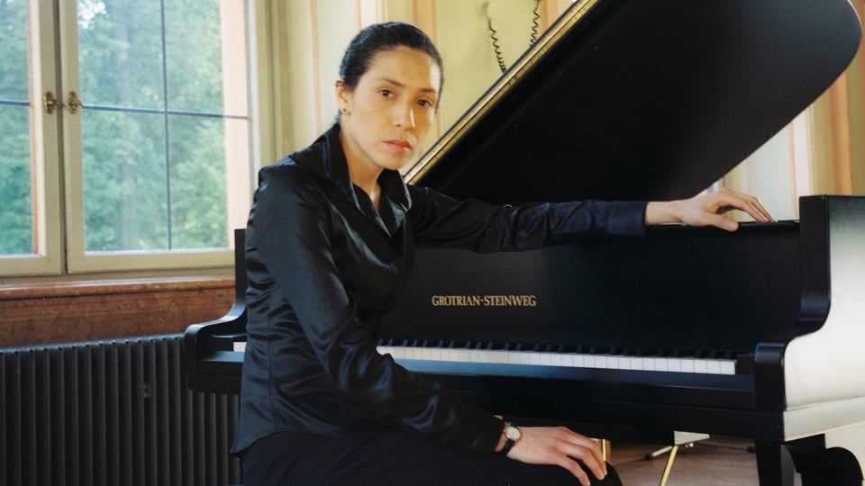 Die Künstlerin in schwarzer Kleidung am Konzertflügel sitzend