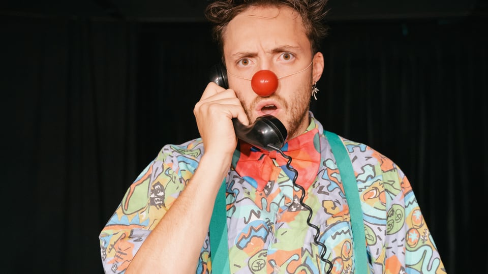 Mann mit buntem Hemd und Clownsnase, einen Telefonhörer in der Hand