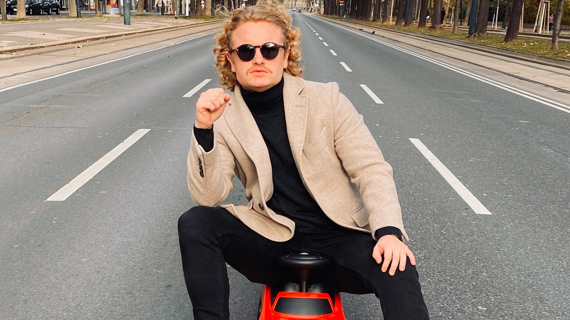 Der Künstler sitzt auf einem Spielzeugauto auf einer Straße