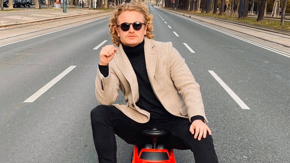 Der Künstler sitzt auf einem Spielzeugauto auf einer Straße