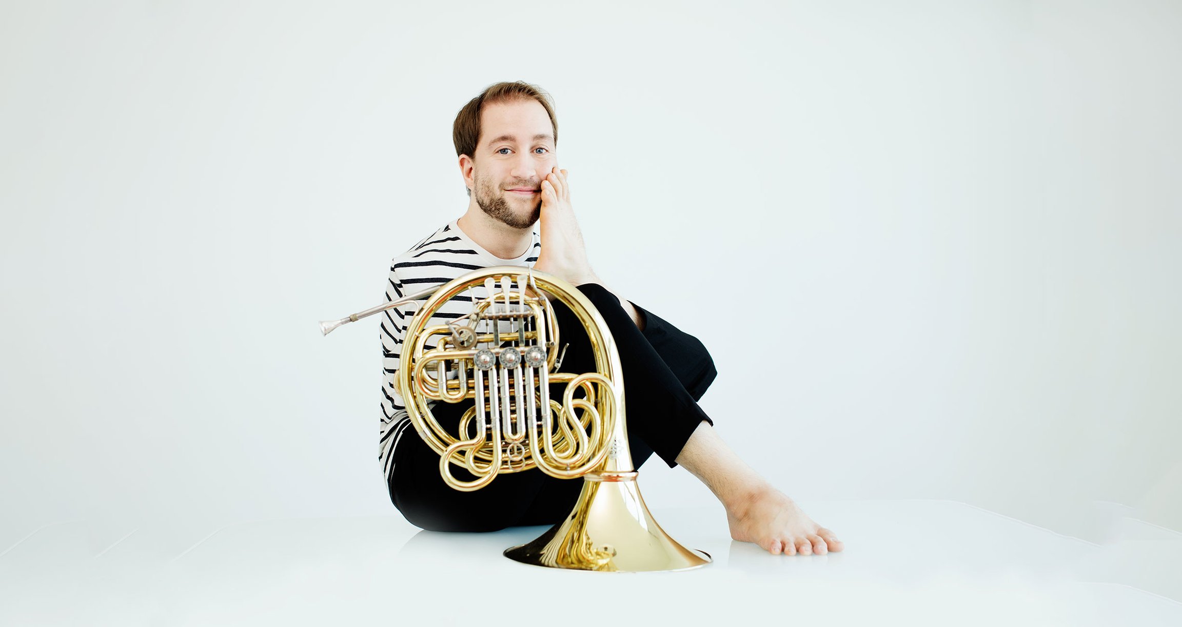 Mann in gestreiftem Shirt mit Instrument auf dem Boden sitzend vor weißem Hintergrund
