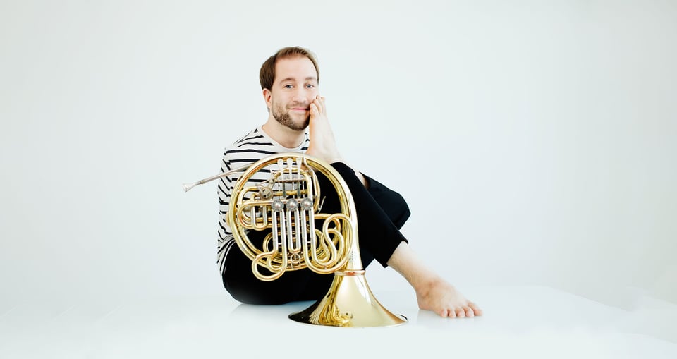 Mann in gestreiftem Shirt mit Instrument auf dem Boden sitzend vor weißem Hintergrund