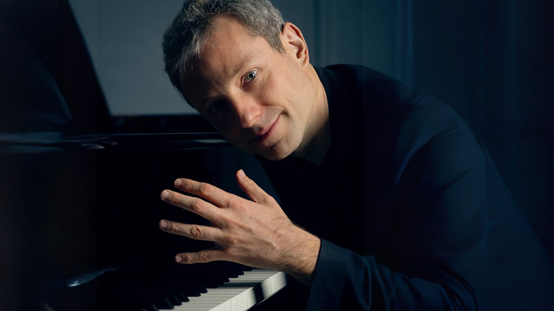 Der Künstler in dunkelblauer Kleidung am Flügel sitzend