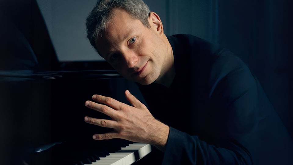 Der Künstler in dunkelblauer Kleidung am Flügel sitzend