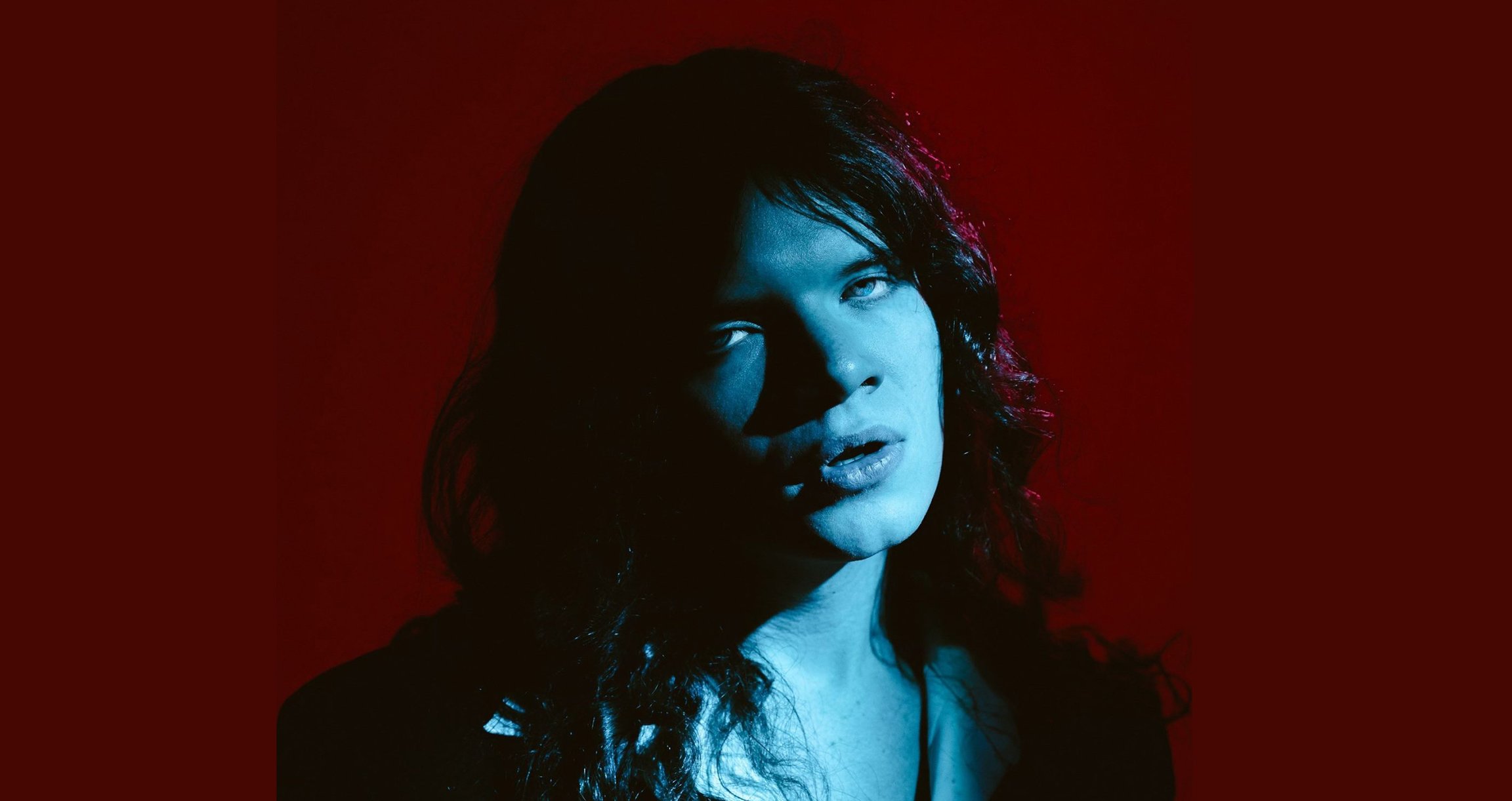 Portrait von Mann mit langen Haaren in blauem Licht mit dunkelrotem Hintergrund