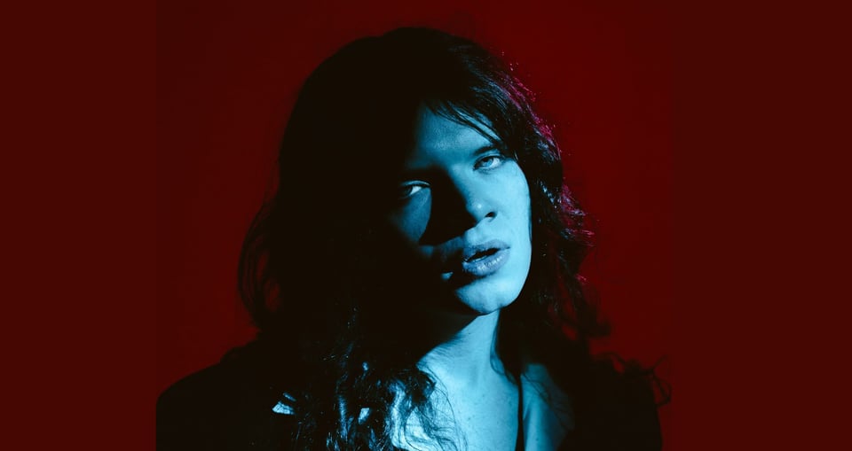 Portrait von Mann mit langen Haaren in blauem Licht mit dunkelrotem Hintergrund