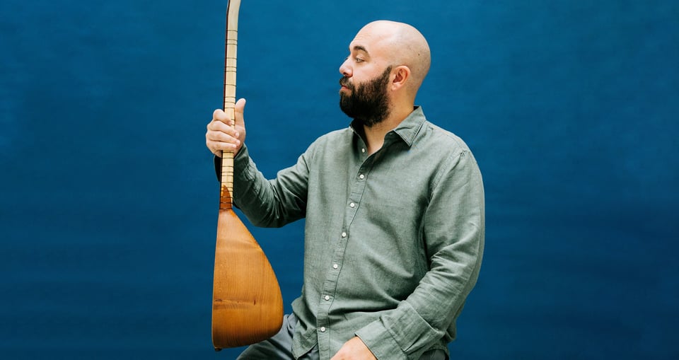 Foto des Künstlers mit einem Instrument vor blauem Hintergrund.