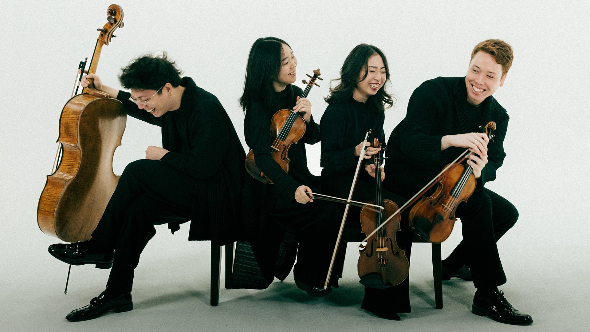 Vier schwarz gekleidete Musike*innen mit Instrumenten auf Stühlen sitzend