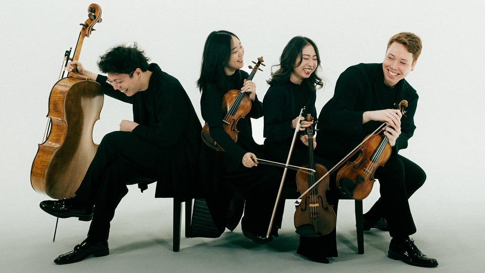 Vier schwarz gekleidete Musike*innen mit Instrumenten auf Stühlen sitzend