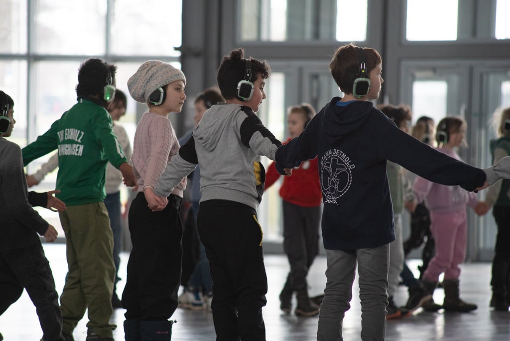 Foto einer Gruppe von Kindern, die Hand in Hand gehen und Kopfhörer tragen