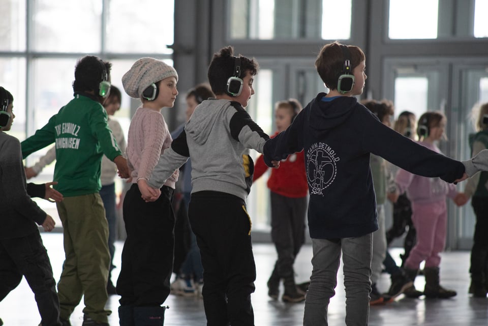Foto einer Gruppe von Kindern, die Hand in Hand gehen und Kopfhörer tragen