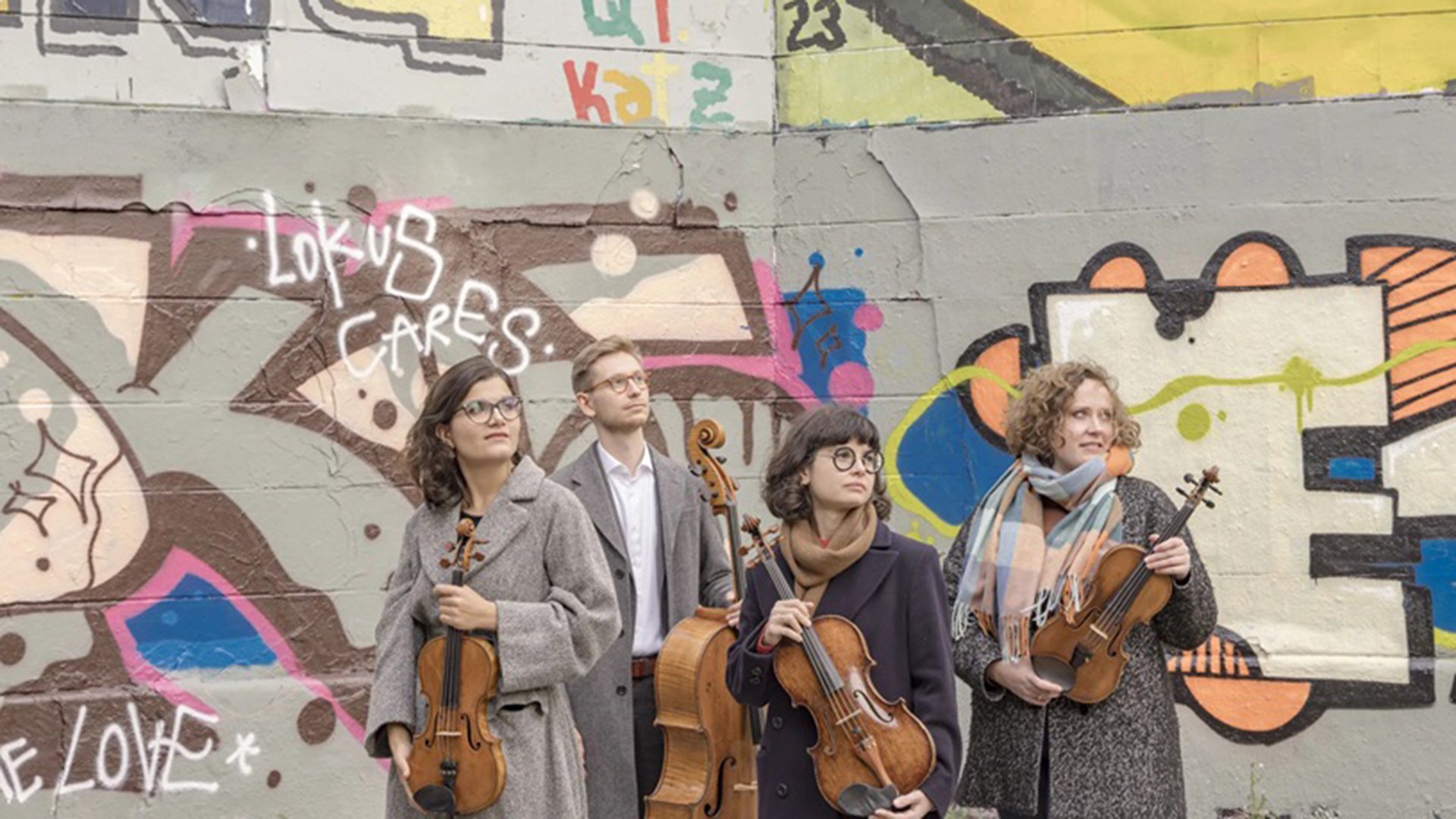 Streichquartett mit vier Musikerinnen und Musikern vor einer bunt bemalten Graffitiwand. Die Mitglieder des Chaos String Quartet halten Violinen und Violoncello und stehen vor urbaner Streetart-Kulisse.