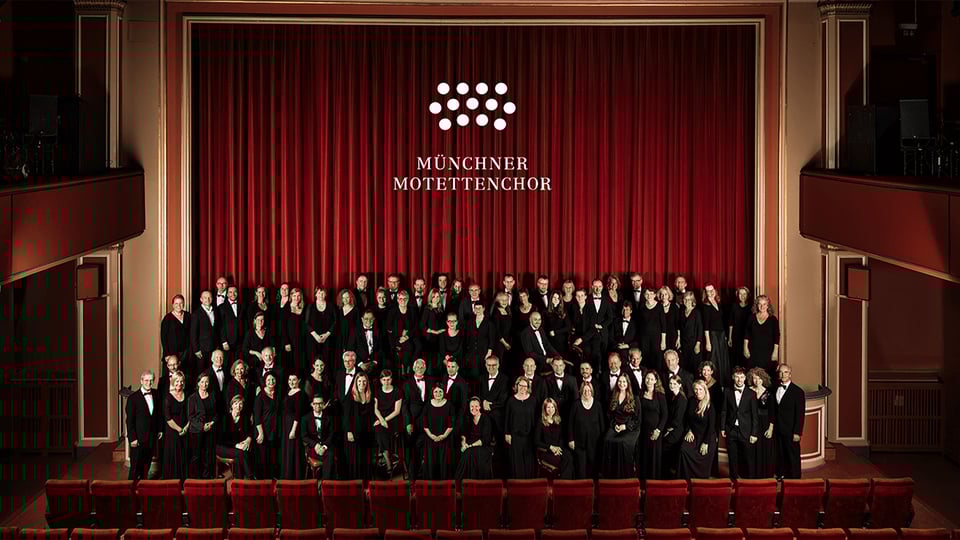 Der Chor in schwarz gekleidet vor der Bühne mit rotem Vorhang