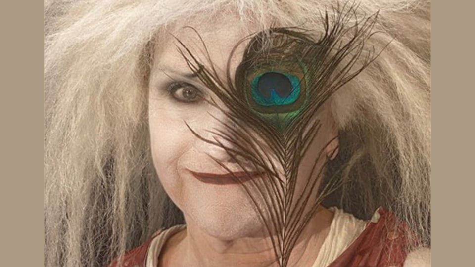 Gardi Hutter mit weiß geschminktem Gesicht, dunklem Lippenstift und wirrem grauem Haar, teilweise verdeckt von einer Pfauenfeder vor dem Gesicht