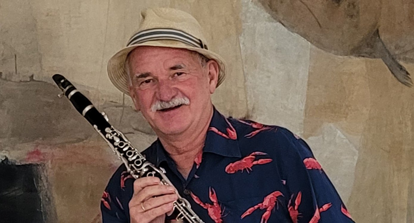 Foto eines Mannes mit einem Instrument in der Hand. Er trägt einen Hut und ein Hemd mit Hummermotiven.