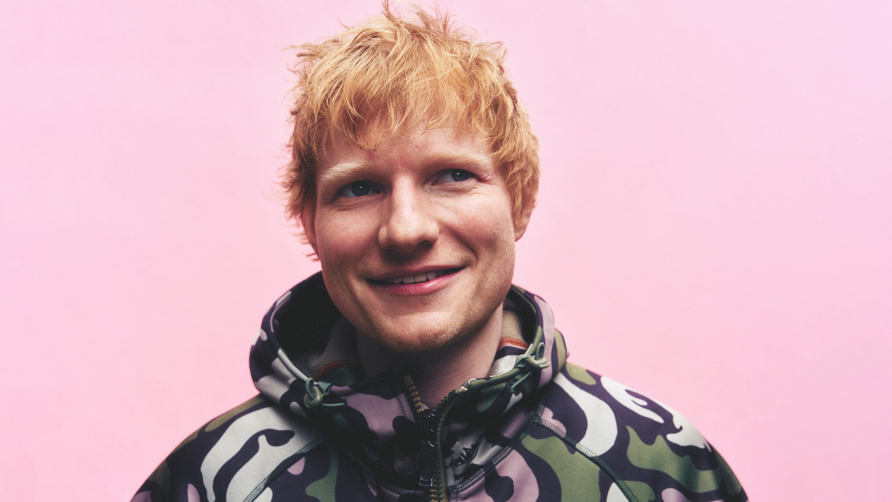 Porträt von Ed Sheeran während er lächelt vor einem rosanen Hintergrund