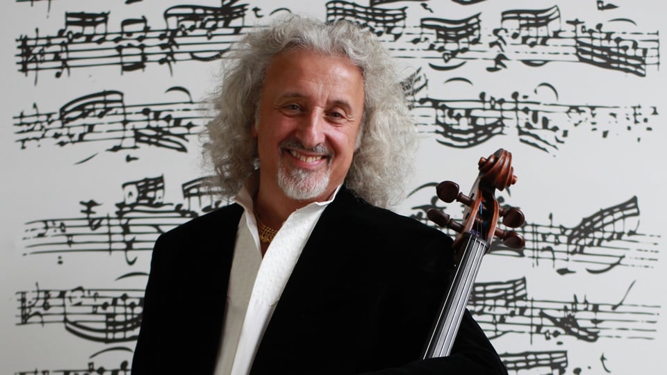 Promobild für das Event ‚Mischa Maisky, Violoncello‘: Eine Person mit lockigem, hellem Haar trägt dunkle Kleidung und hält ein Violoncello. Im Hintergrund sind großformatige, schwarz gedruckte Notenlinien und musikalische Zeichen zu sehen.