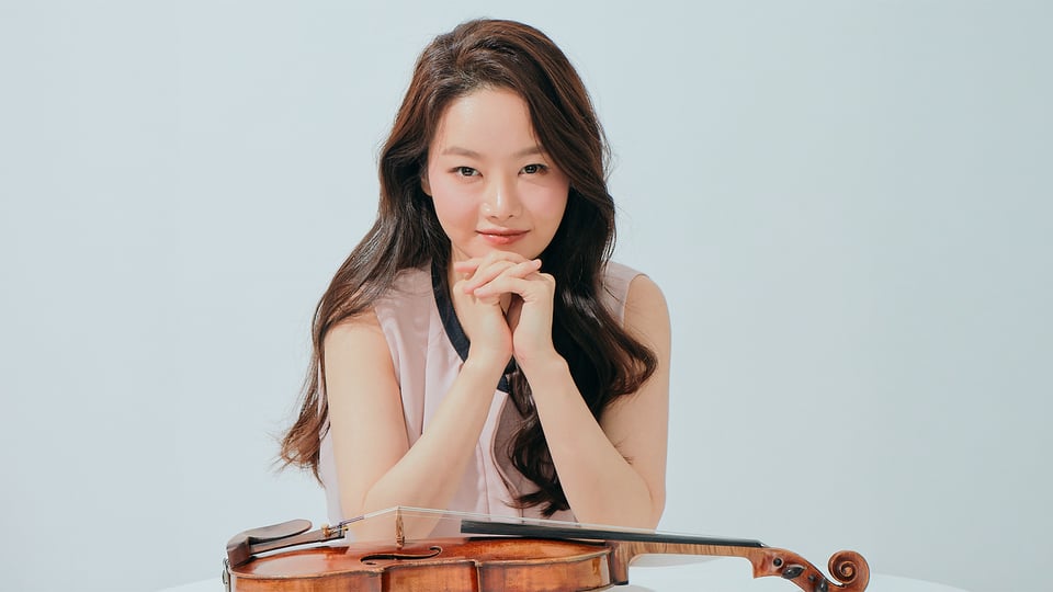 Porträt einer Musikerin mit Violine, lehnt die Hände auf das Instrument vor hellem Hintergrund.
