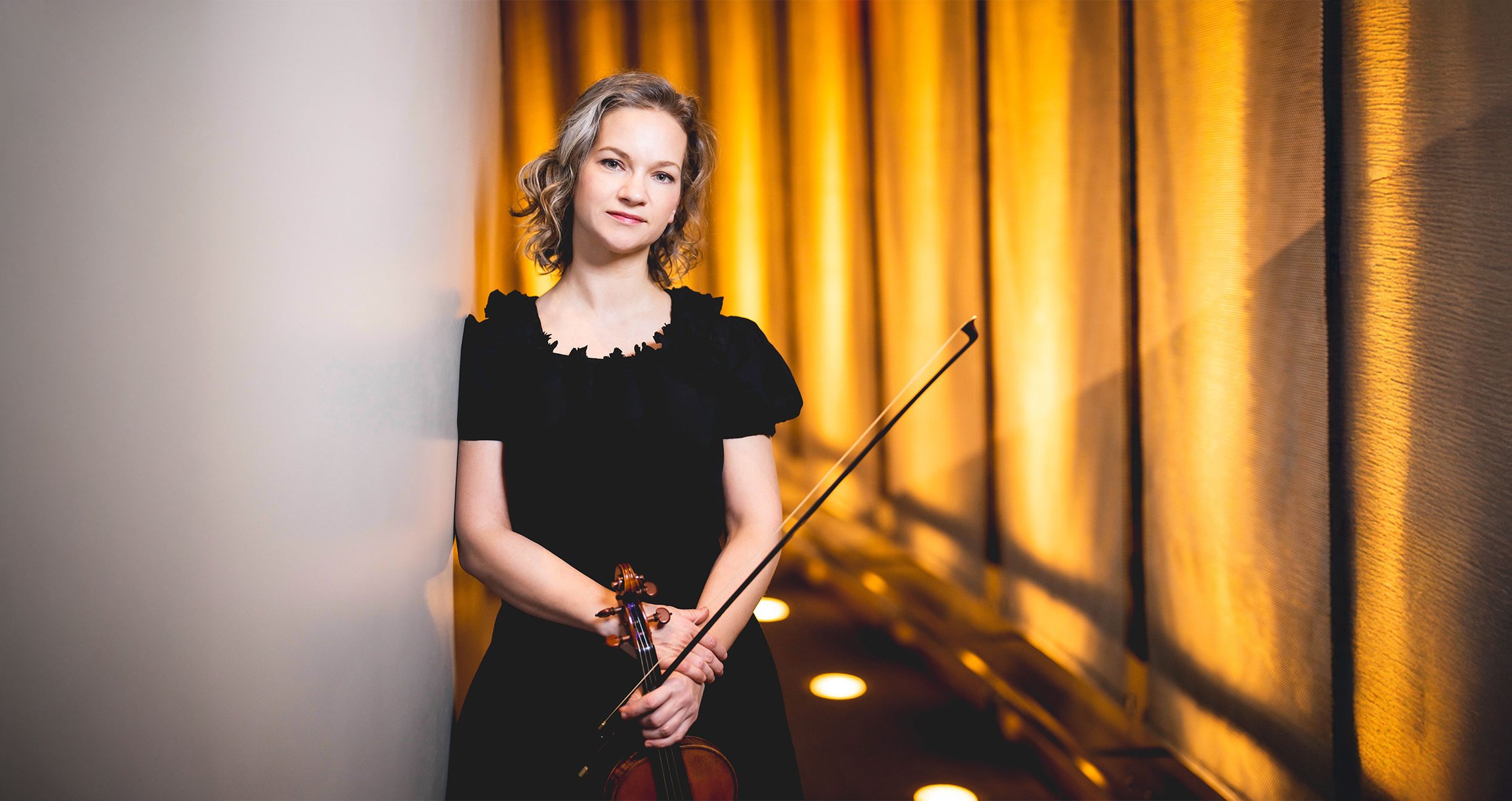 Dame in schwarzem Kleid mit Violine vor gold glänzendem Vorhang