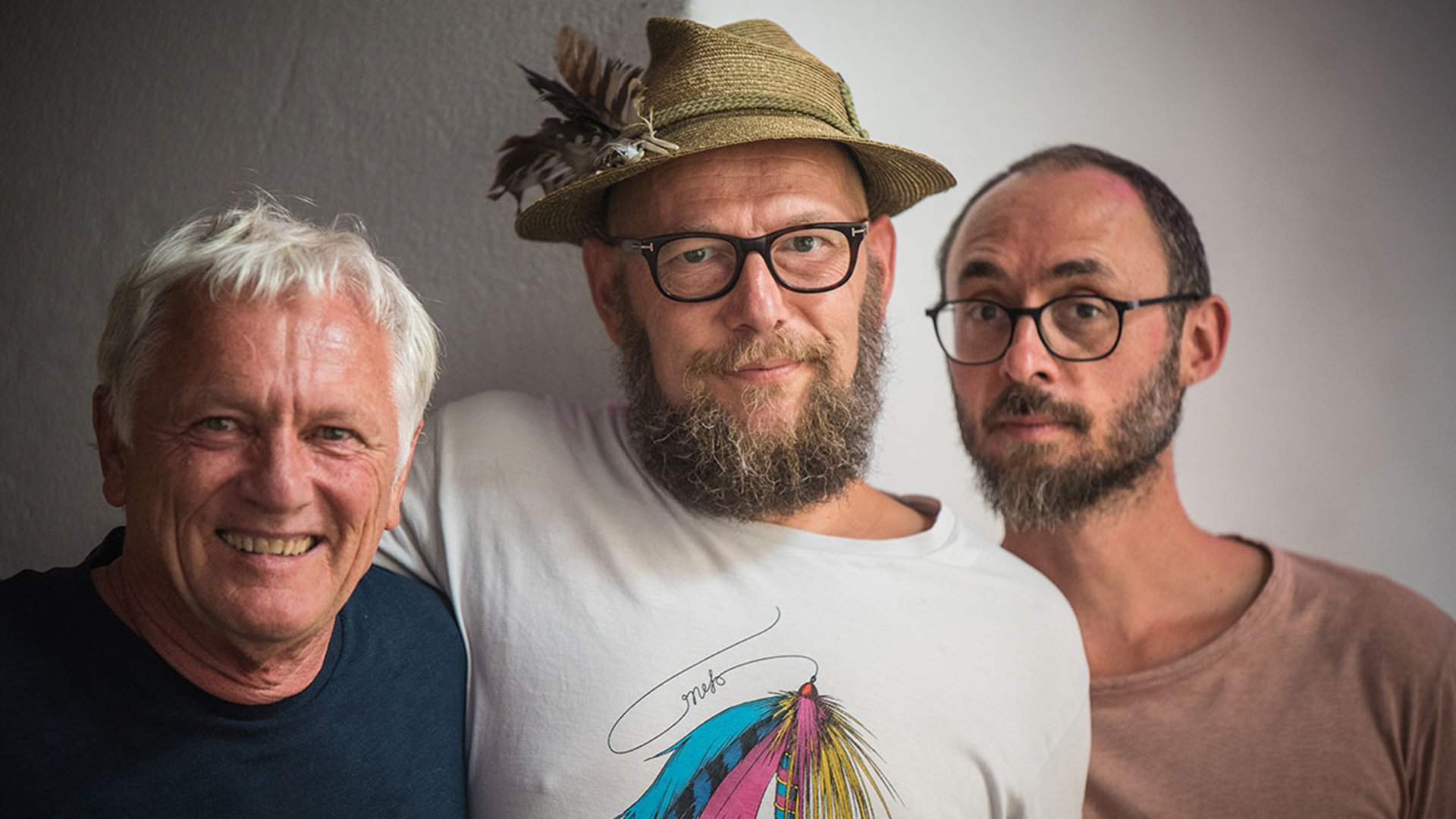 Drei Herren in farigen Tshirts, einer mit Strohhut