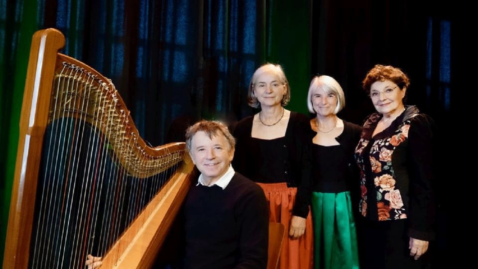 Gruppenfoto von vier Musikerinnen und Musikern neben einer großen Harfe vor dunklem Bühnenvorhang. Eine Person sitzt vor dem Instrument, während drei weitere Personen dahinter stehen und traditionelle Konzertkleidung tragen.