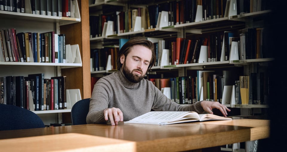 Mann an Schreibtisch in Buch lesend mit Bücherregal im Hintergrund