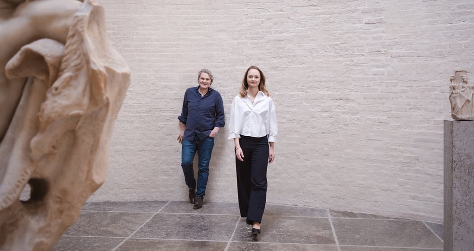 Eine Dame und ein Herr vor einer Mauer, auf den Seiten historische Statuen
