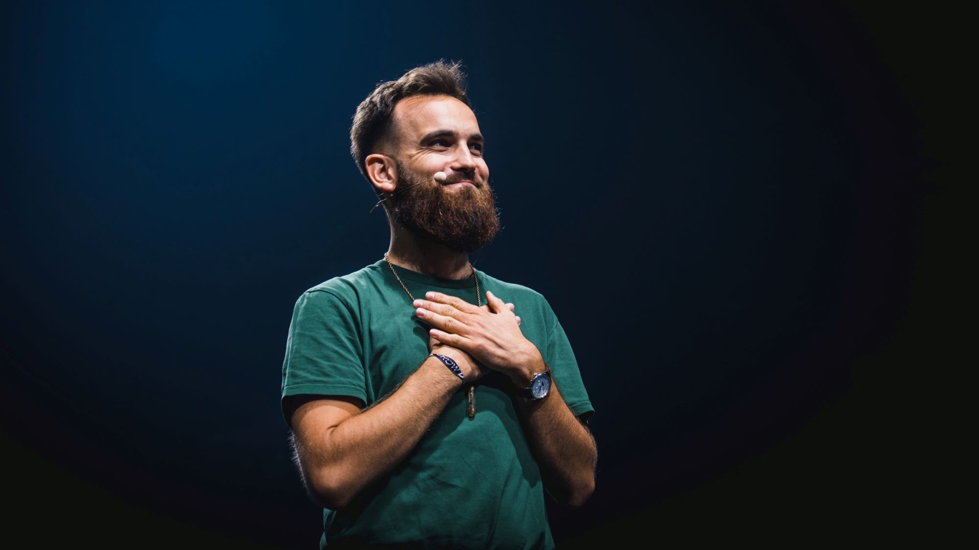 Maik Baum mit gekreuzten Händen in einem dunkelgrünen Shirt vor dunklem Hintergrund