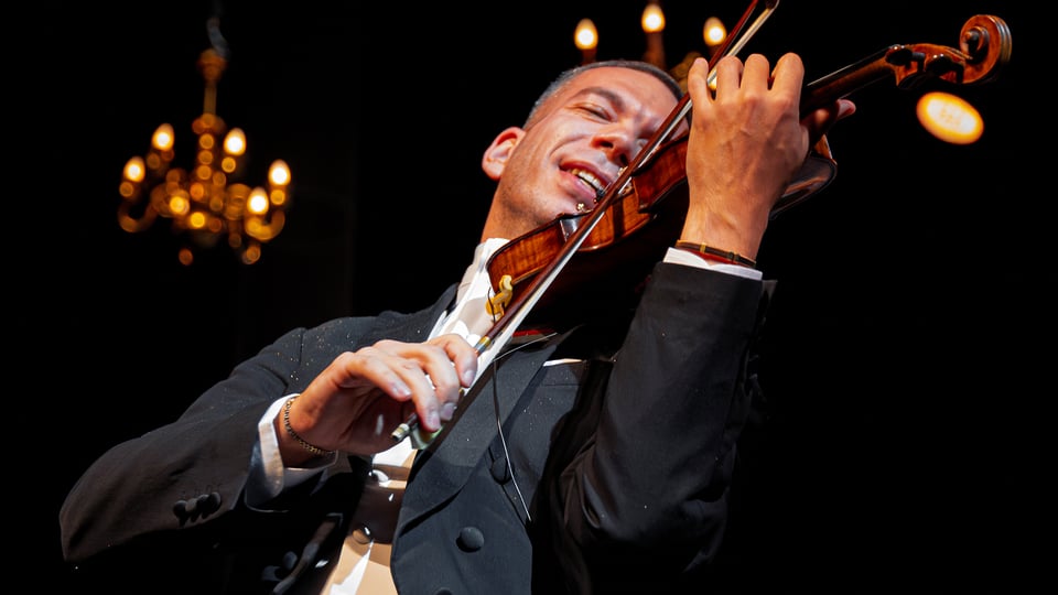 Der Dirigent und Geiger Bogdan Alexandru Costache in dunklem Anzug mit Instrument auf der Bühne, im Hintergrund Kronleuchter