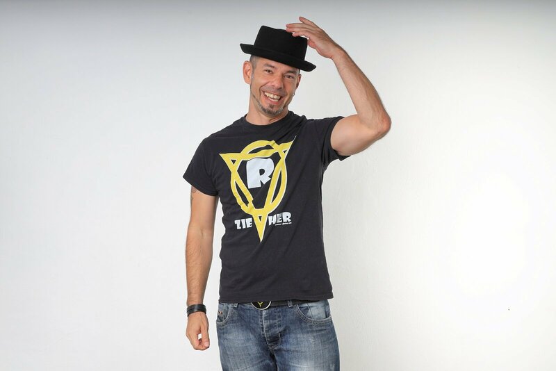 Der Künstler in schwarzem Shirt, Jeans und Hut vor hellem Hintergrund