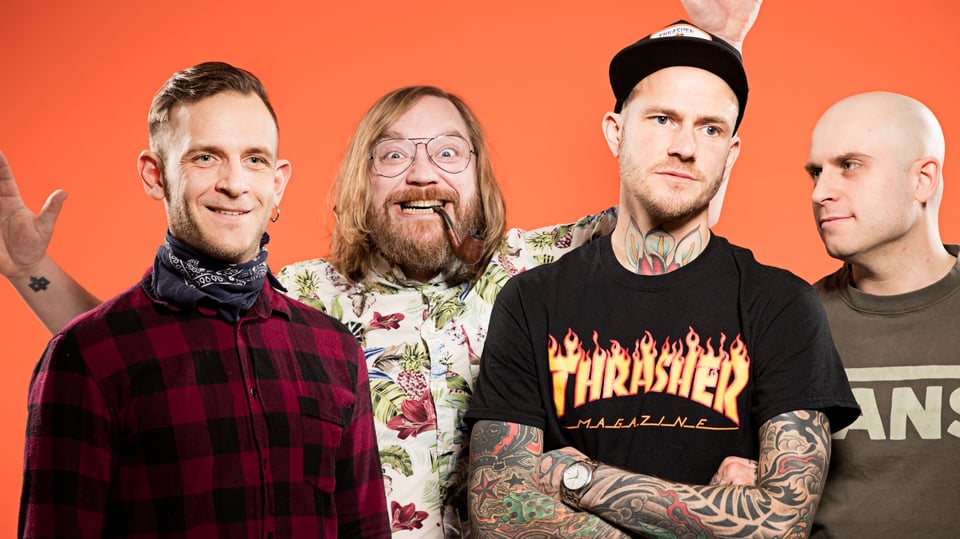 Vier Männer in farbiger Kleidung vor orangem Hintergrund