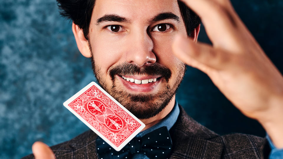 Nahaufnahme eines Magiers mit Spielkarte vor blauem Hintergrund, Porträtbild für eine Zaubershow mit Kartenzauber.