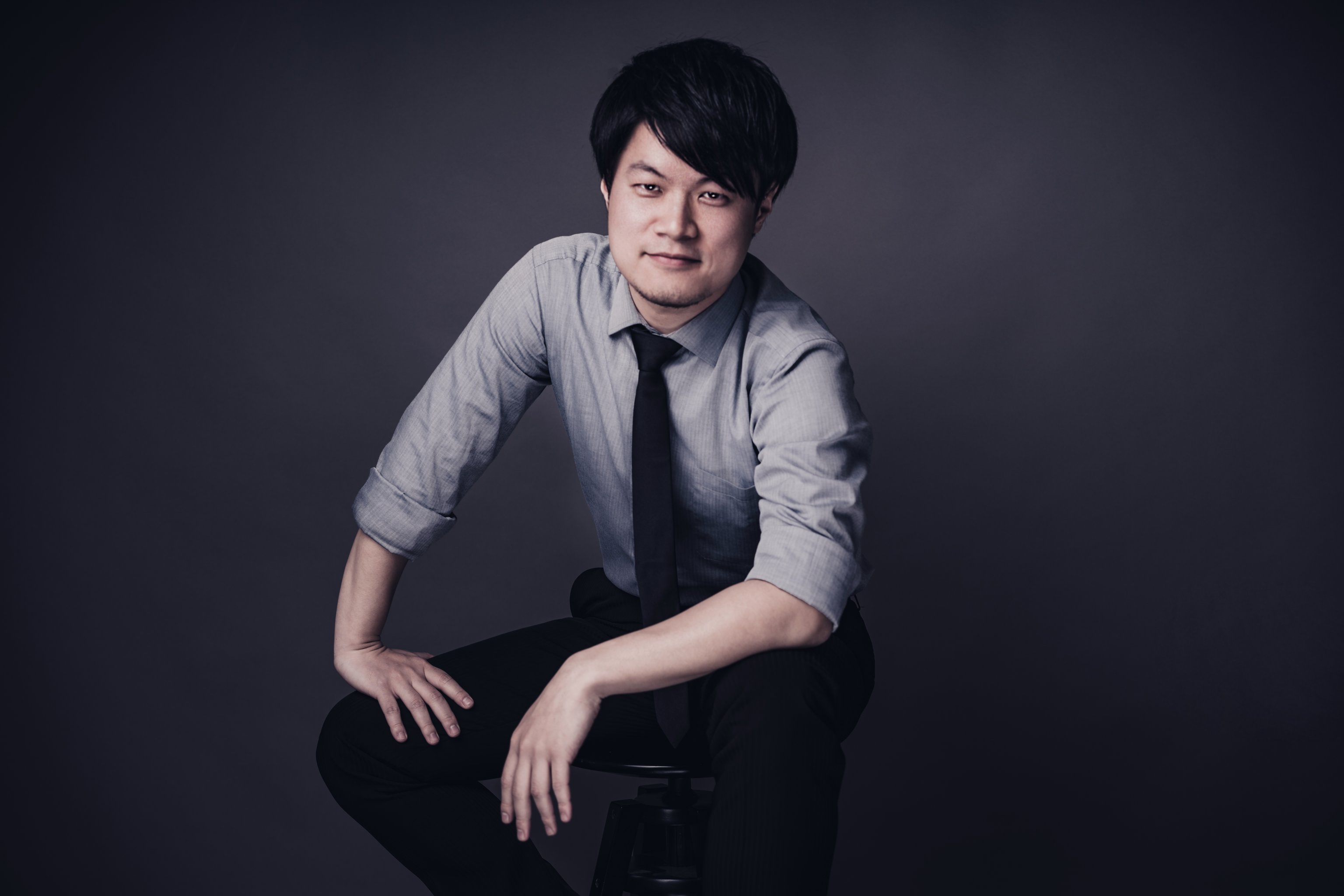 Der Pianist Yuto Kiguchi in grauem Hemd auf einem Klavierstuhl sitzend