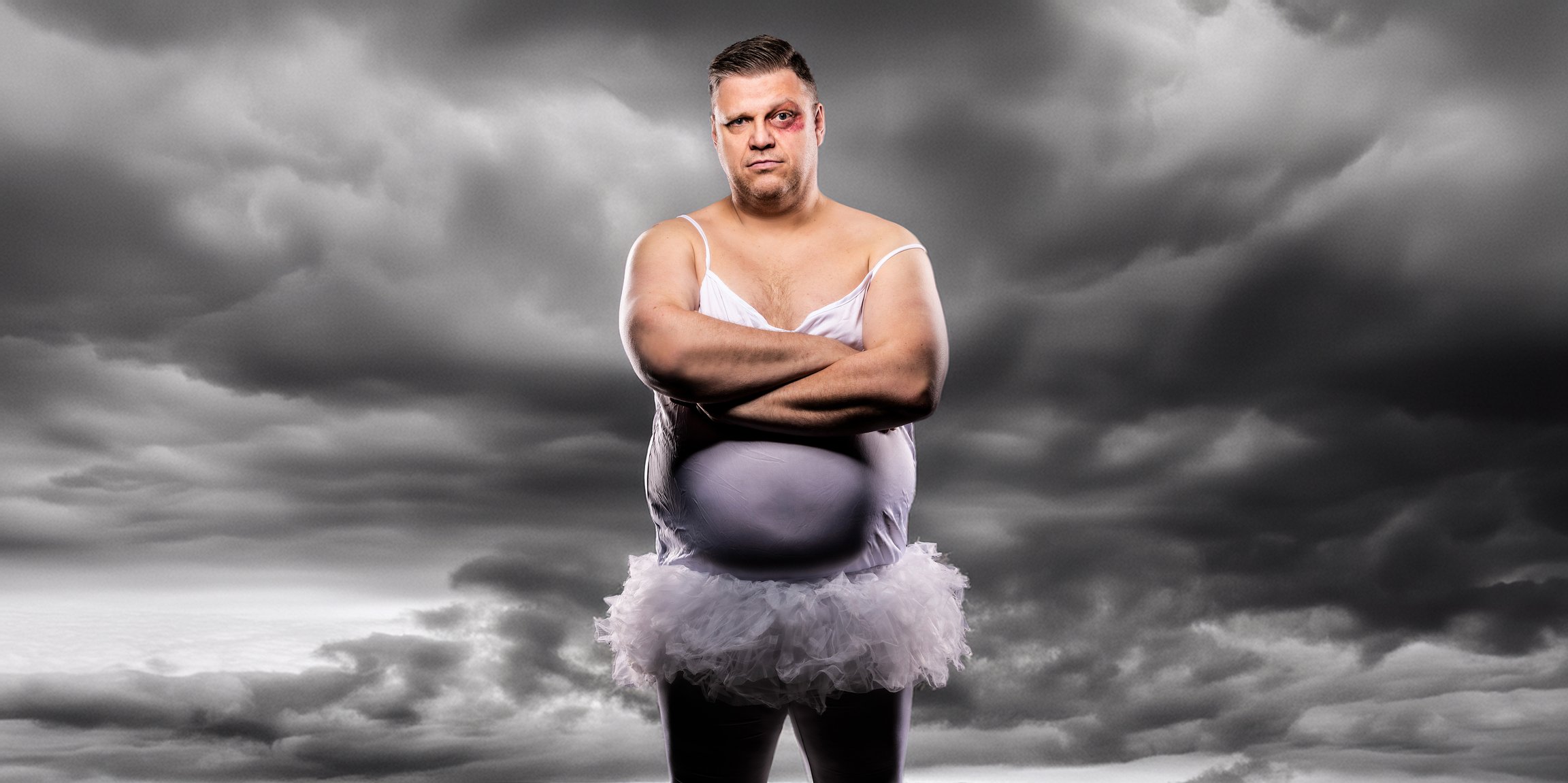 Foto von „Ralf Winkelbeiner“ im fliederfarbenen Kleid mit einem blauen Auge. Im Hintergrund graue Wolken