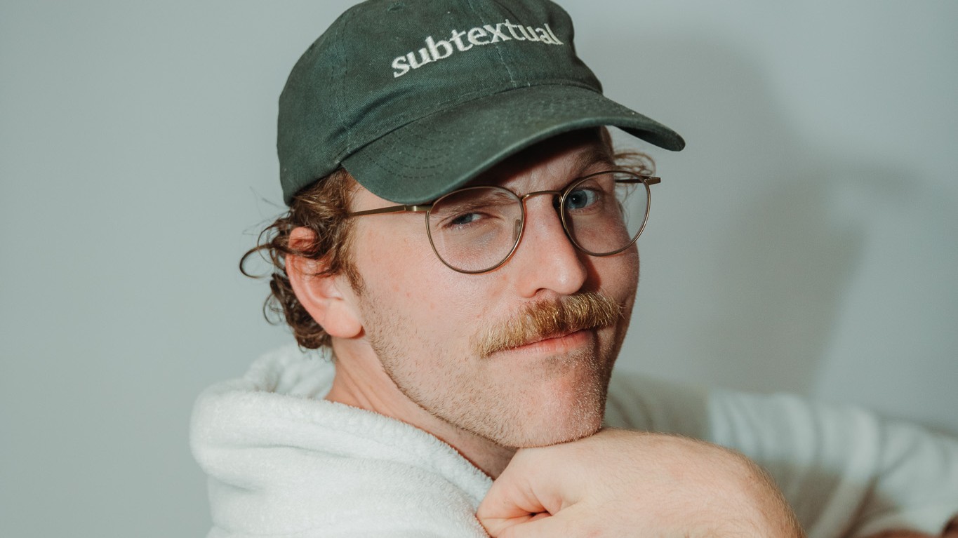 Portrait von Jordan Prince in weißem Pullover mit grüner Kappe blickt lächelnd in die Kamera vor hellem Hintergrund