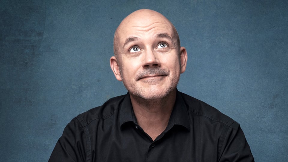 Portrait von Frank Fischer vor einem blauen Hintergrund wie er den Blick nach oben gerichtet hat