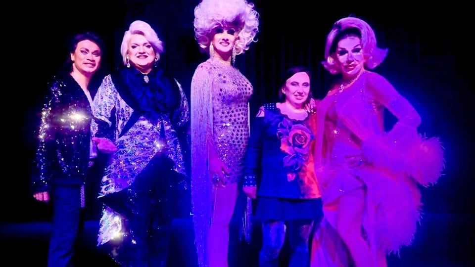 Fünf darsteller*innen auf der Bühne in lila und pinkem Scheinwerferlicht